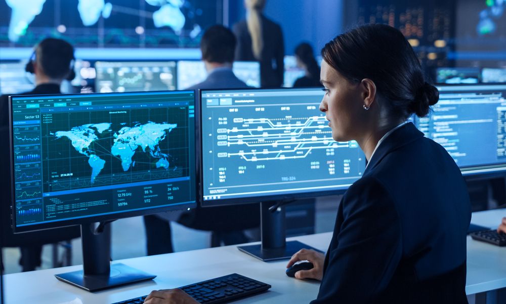 Team Of Professional Computer Data Science Engineers Work On Desktops With Screens Showing World Map, Charts, Graphs Infographics Technical Business Data And Statistics. Dark Control Monitoring Room.