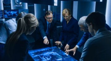 Team Of Government Intelligence / Fbi Agents Standing Around Digital Touch Screen Table And Tracking Suspect Vehicle Using Satellite Surveillance In The Monitoring Room.